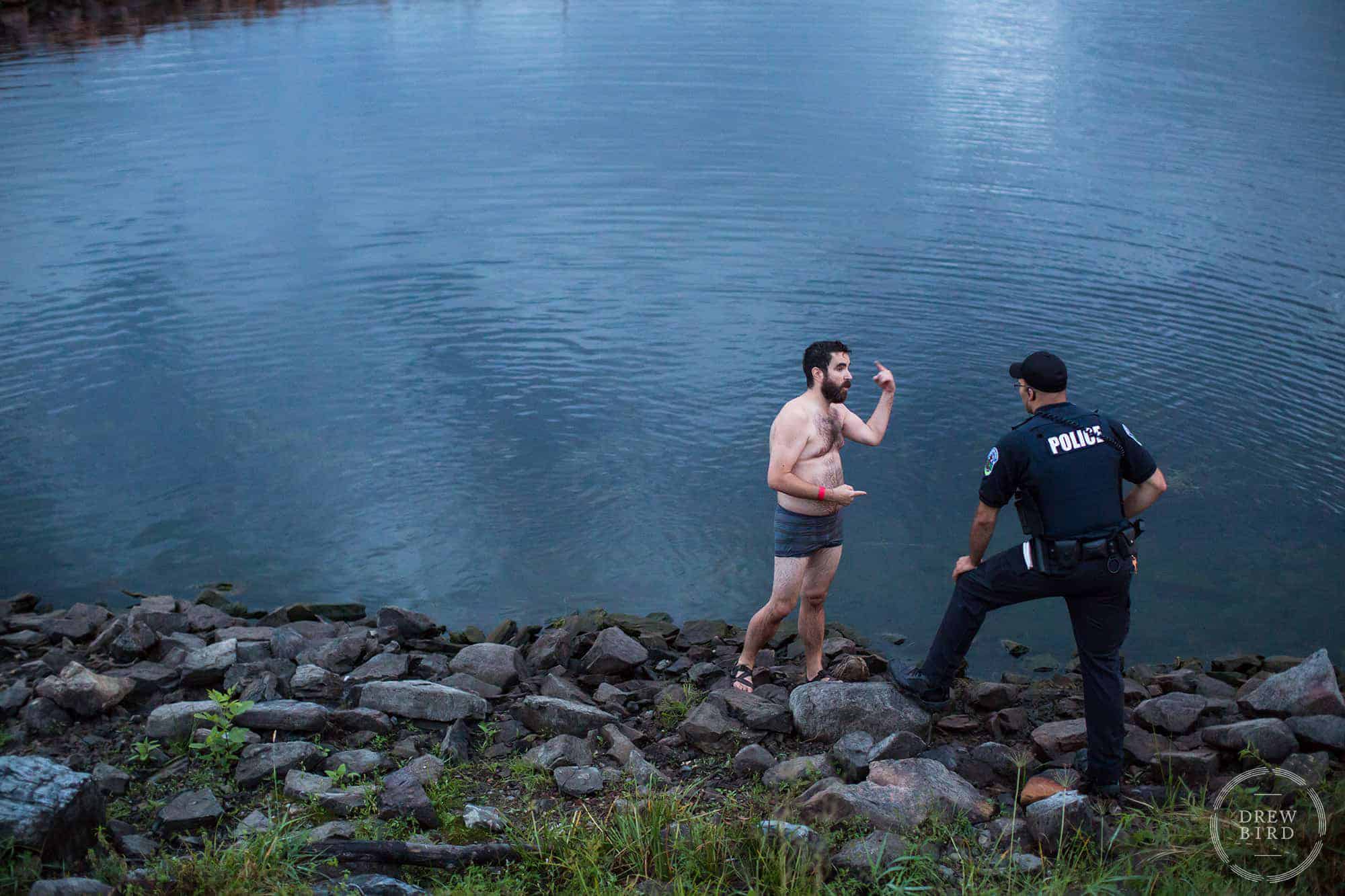 Uniformed police officer talking to a man wearing shorts and sandals next to the water. Editorial photography by Drew Bird Photo, a San Francisco based photographer.