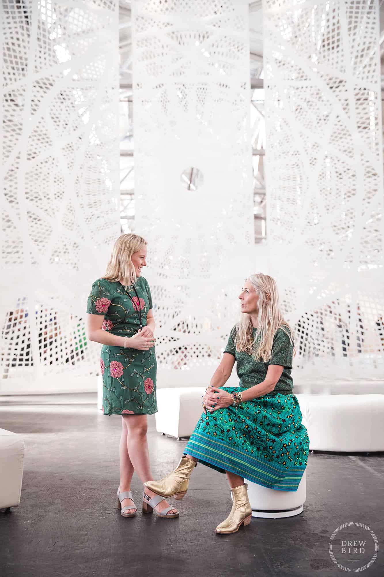 Two attractive women with blond hair and green dresses talking at Fort Mason festival pavilion. San Francisco corporate lifestyle and event photographer Drew Bird.