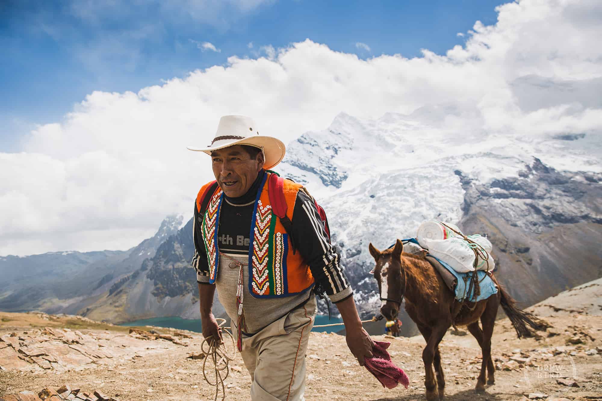 A mountain guide leads a pack horse with Ausangate tropical glacier in background in the mountains of Peru. San Francisco Editorial Photographer Drew Bird.