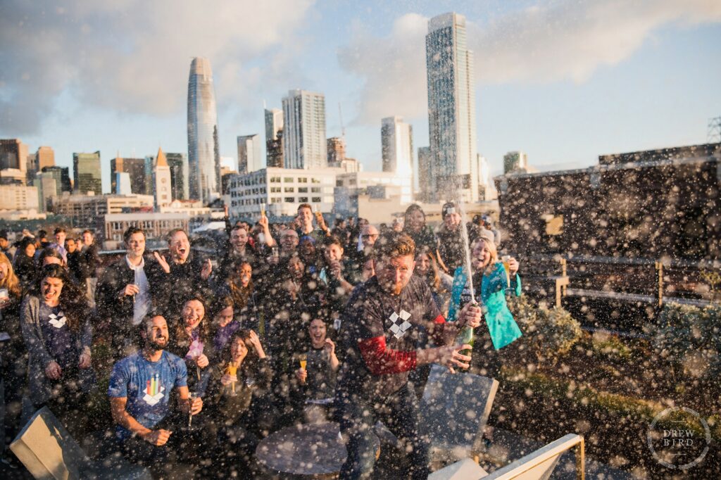 Dropbox IPO corporate lifestyle photo project. Champagne celebration at sunrise on the rooftop garden at Dropbox HQ with San Francisco skyline. Commercial photographer Drew Bird.